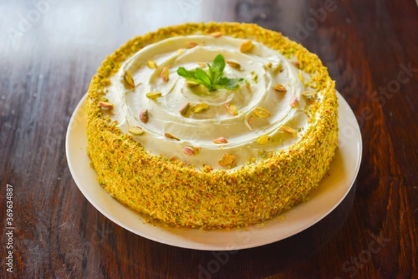 Fototapeta Sweet pistachio dessert with vanilla cream and nuts on white plate. Slice of pistachio cake. Tea time.