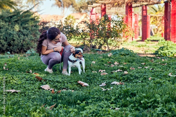 Obraz young woman wearing a safety mask in the park with her dog petting him in the middle of the covid 19 pandemic