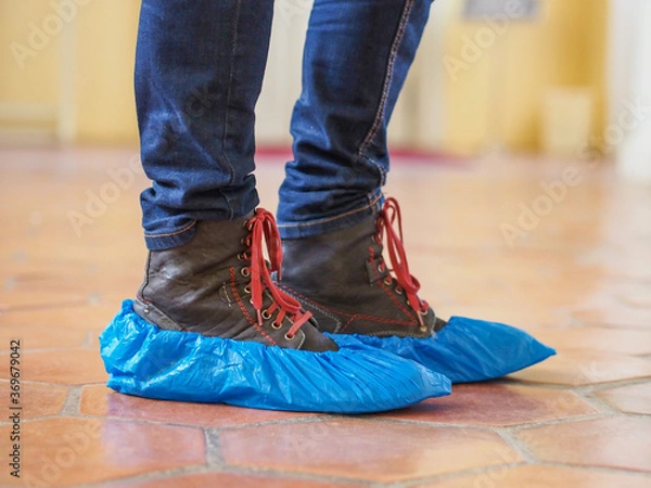 Fototapeta Man with blue shoe covers worn over boots with red shoe laces standing on a tiles, closeup side view.