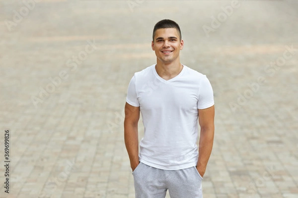 Fototapeta A young man in a sports uniform stands in the park.