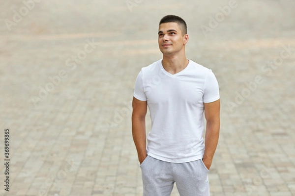 Fototapeta A young man in a sports uniform stands in the park.