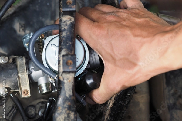 Fototapeta Man replacing the scooter's carburetor with a new one.