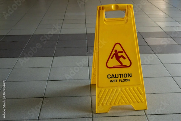 Fototapeta Wet cleaning of the room on the wet tile floor is a yellow stand with the inscription "careful slippery floor". Copy space.
