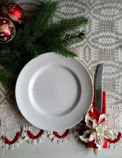 Fototapeta Christmas table setting. a knife and a fork laid out on a linen tablecloth wrapped in a red napkin on a white plate. 