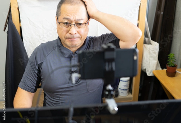Obraz スマートフォンをウェブカメラにしてオンラインミーティング中に頭を抱え困っている男性