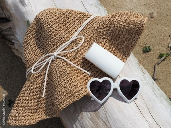 Fototapeta ビーチの必需品、流木の上に置かれたストローハットとサングラスと日焼け止め