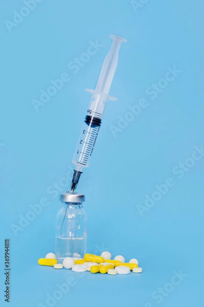 Fototapeta a syringe stuck in a medicine bottle and a lot of pills near by on a blue background