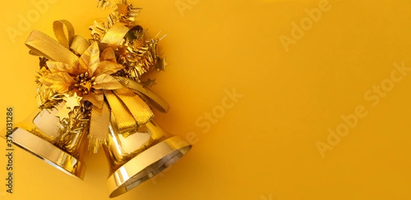 Fototapeta Gold Christmas bells with ribbons and poinsettia on a yellow background with copy space. Close-up, top view, horizontal position, banner