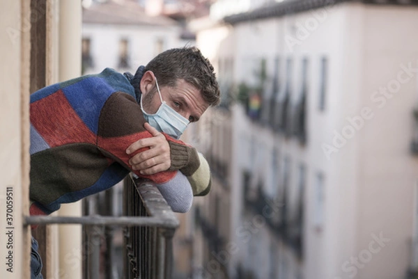 Fototapeta stay home quarantine portrait of of 30s handsome man in face mask sad and depressed at home balcony during covid19 lockdown feeling worried and scared