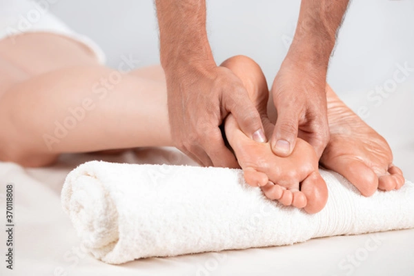 Fototapeta The masseur massages the pads of the feet of the girl who is lying on the massage table. Very close-up, soft light pastel light tones.