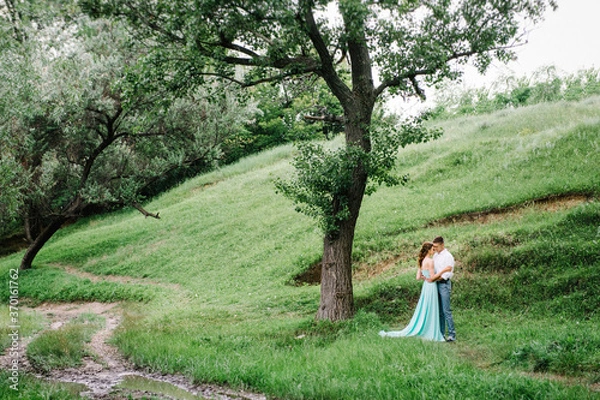 Fototapeta happy guy in a white shirt and a girl in a turquoise dress are walking in the forest park