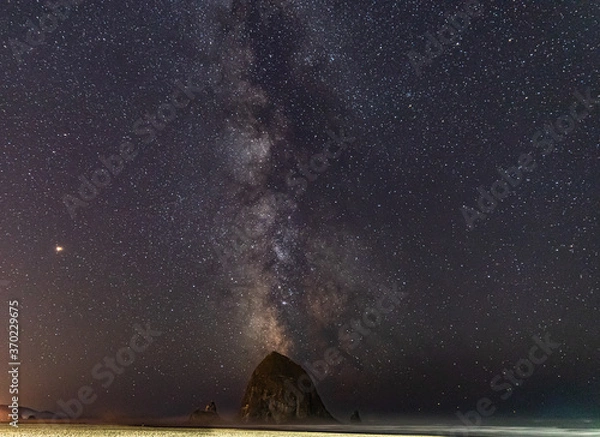 Obraz Milky Way galaxy shines in the sky behind Haystack Rock on Cannon Beach in Oregon