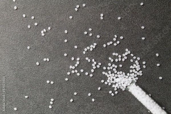 Fototapeta Plastic pallets. White Polyethylene granules spilled out of a laboratory test tube on a stone background. Plastic Raw material .High Density Polyethylene.