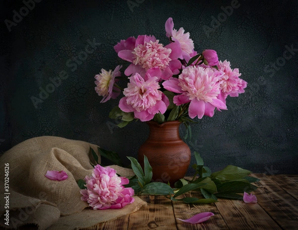 Fototapeta A bouquet of peonies stands in a clay jug on a wooden table.