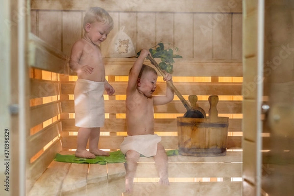 Fototapeta Kids are steaming in the Russian bath. Two kids with a bucket and a basin in the sauna. Twin boys relax in the bath. Сute children in the sauna on a wooden shelf. Steam and heat in the Russian sauna