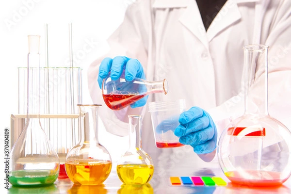 Fototapeta Chemical show. Demonstration of experiments with multicolored chemical liquids. Mixing of substances in test tubes. Chemist's hands close up. Laboratory glassware.