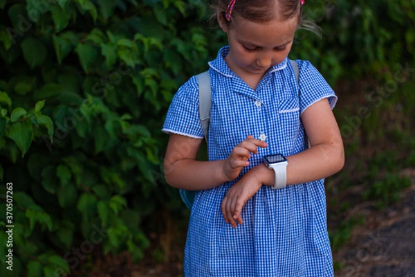 Fototapeta Kid using smartwatch outdoor in park. Child talking on vdeo call on the smartphone. Schoolgirl using touchscreen display on watches browsing internet. Smart wristwatch with GPS tracker.