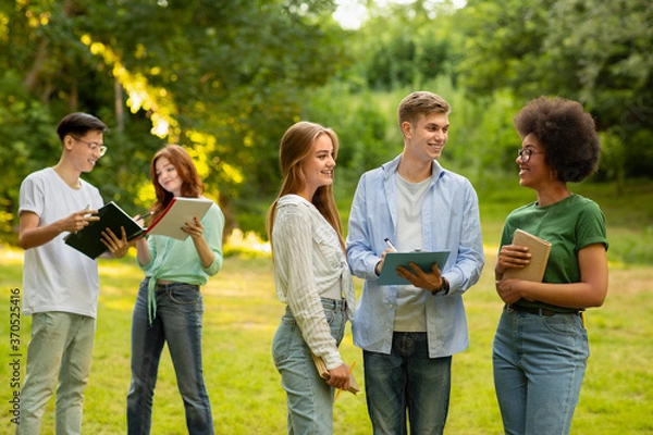 Fototapeta University students resting outdoors at campus after classes, chatting and smiling