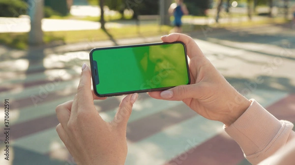 Obraz NEW YORK - 5 April 2018: Close up of woman hands holding and touching phone with green screen horizontal in the street people crosswalk background internet technology business message slow motion