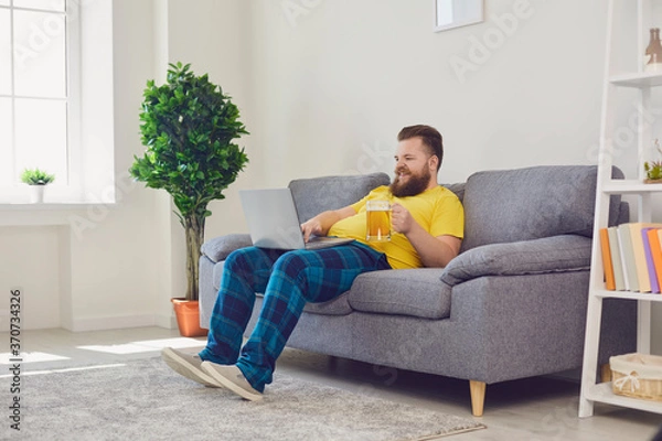 Fototapeta Online communication. Funny guy with beer chatting to friends on laptop from home. Bearded man making video call