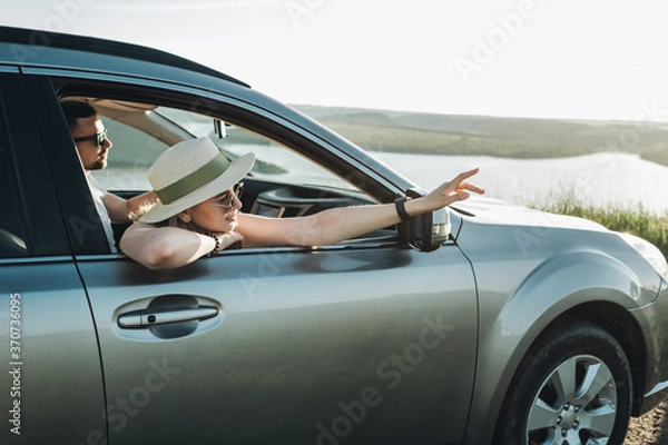 Fototapeta Happy Young Couple Sitting Inside Their Car and Enjoying Road Trip, Travel and Adventure Concept