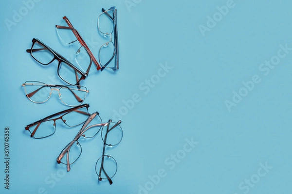 Fototapeta Set of corrective medical eyeglasses of various shapes lying on blue background with copy space