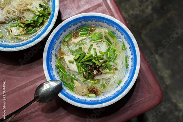 Obraz  Soup called hu tieu go (noodle, meat products, herbs) on a shabby red plastic table in the street in Ho Chi Minh City, for 15 000 dongs (0.65 USD) a bowl. A budget food popular in Saigon, Vietnam.