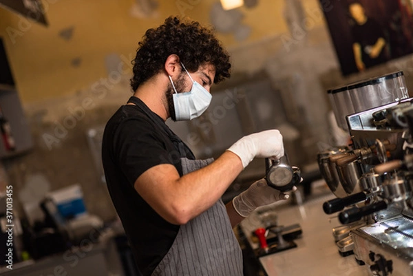 Fototapeta Young man, barista, making coffee espresso while wearing surgical mask and gloves for preventing corona virus spread - Bar safety working concept.