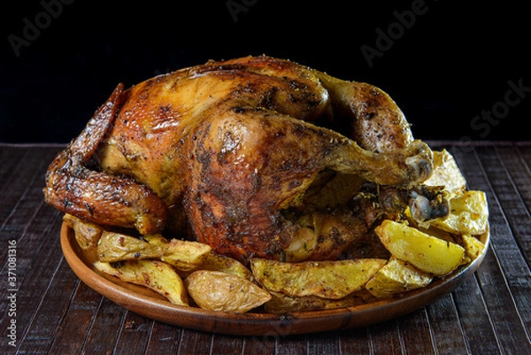 Fototapeta Peruvian food: "Pollo a la brasa con papas fritas" or grilled chicken with french fries and creams on wooden plate.  Black background.