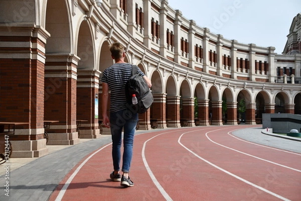 Obraz A young blond caucasian male model is going forward with his backpack at the stadium, concept for moving on and not looking back