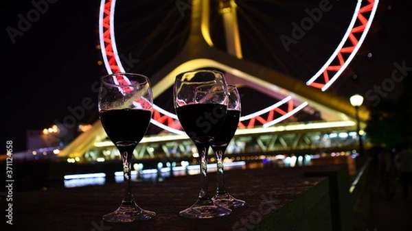 Obraz three glasses with wine with ferry's wheel at the background at night from the low angle