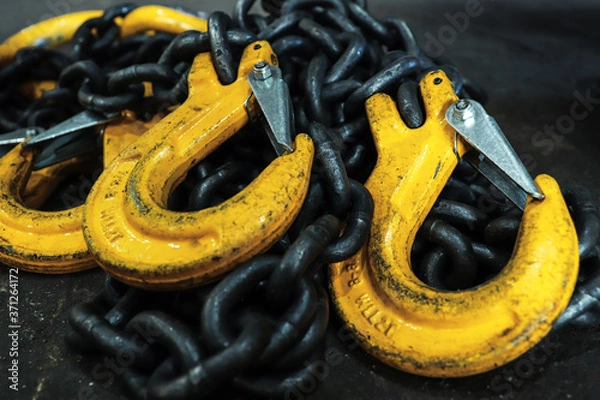 Fototapeta Iron chains with hooks lie on the floor of the workshop. A device for loading and unloading goods.