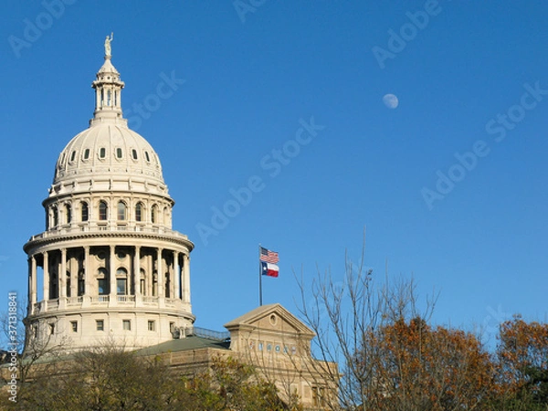 Fototapeta the Capitol of Texas with a three quarter moon and a stiff breeze blowing on the US and State flags
