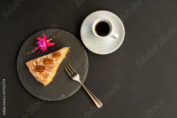 Obraz A typical Portuguese cake made of cookies called Bolo de Bolasa with cream, pecans, black and white chocolate on a black slate with a fork, espresso and a flower on a black background.Top view Flatlay