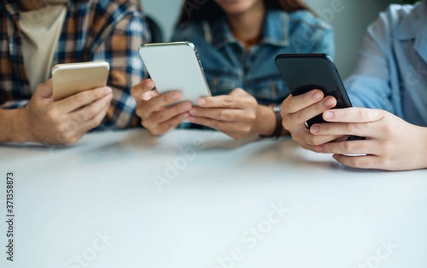 Fototapeta Group of young people using and looking at mobile phone while sitting together