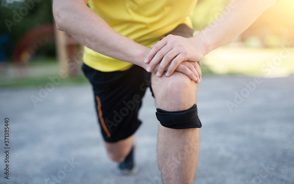 Obraz Man exercising lunges with protective knee bandage, close up