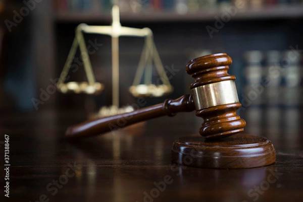 Fototapeta Law theme. Judge chamber. Gavel and scale on brown shining desk. Collection of legal books in the bookshelf.
