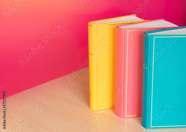 Fototapeta Simple composition of hardback multicolored books, raw of books on pink background. Books stacking with no labels, blank spine Back to school Copy Space Education background Office supplies