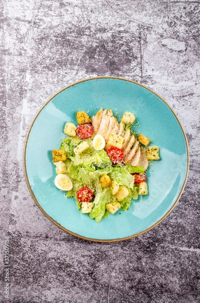 Obraz Fresh Caesar salad with grilled chicken, romaine salad leaf, cherry tomato, quail eggs and parmesan cheese on gray background copy space. Top view. Flat lay
