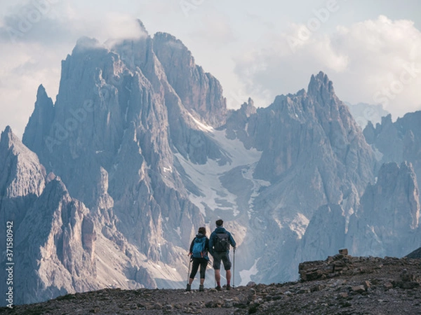 Obraz Couple of hikers standing and admiring stunning beauty of impressive jagged peaks of Cadini di misurina mountain group in Dolomites, Italy, part of Tre Cime di Levaredo national park