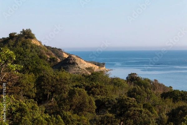 Obraz Scenic landscape wild nature with rocky mountains overgrown dense green trees and clear azure water of sea ocean at sunny day on background beautiful blue sky