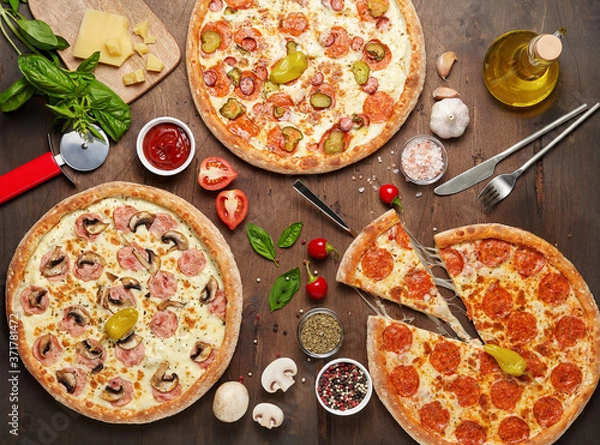 Fototapeta Three hot cheese pizzas with chorizo and mushroom on rustic wooden table with ingredients