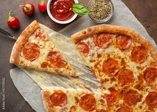 Fototapeta Slice of hot pizza with melting cheese and chorizo on rustic wooden table with ingredients