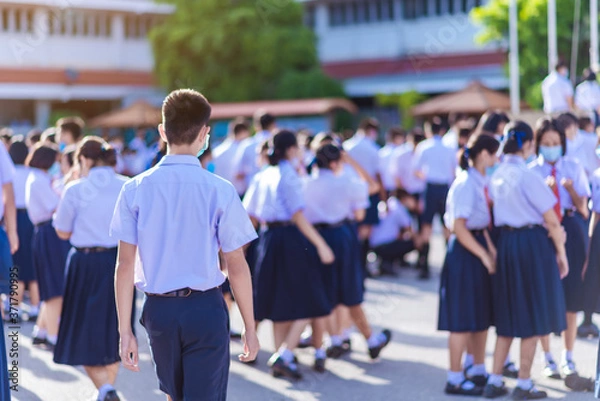 Fototapeta The back view of Asian high school students in white uniforms on the semester start wearing masks during the Coronavirus 2019 (Covid-19) epidemic.