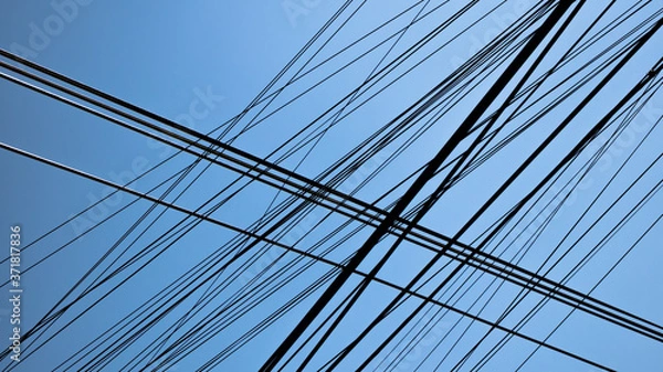 Obraz Hundreds of black communication cables crossing with blue sky behind, wire disorder