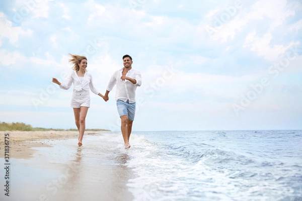 Fototapeta Happy couple running on beach, space for text. Romantic walk
