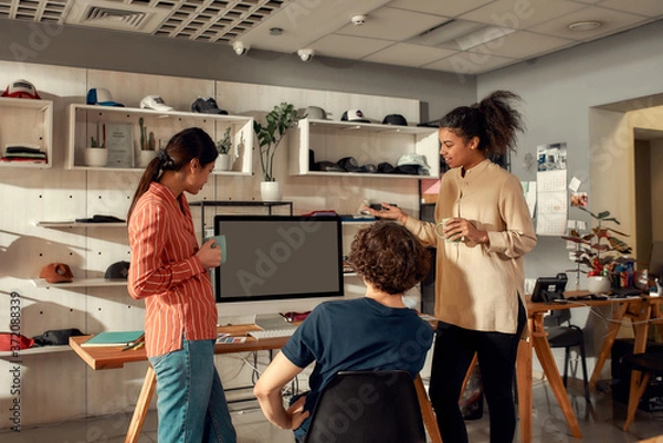 Fototapeta Passion, quality, innovation. Portrait of smiling workers drinking coffee and discussing ideas. Young man and women drawing sketches logo design, working at custom T-shirt, clothing printing company