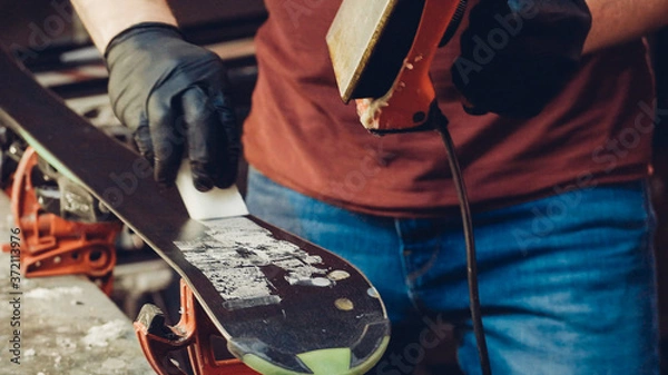 Fototapeta Applying hot wax to ski base with iron. Applying Ski Wax To Ski Base. Ski base tuning. Ski wax iron and wax bars. Ski service and repair. repairman in workshop ski service. Man Waxing Ski In Workshop