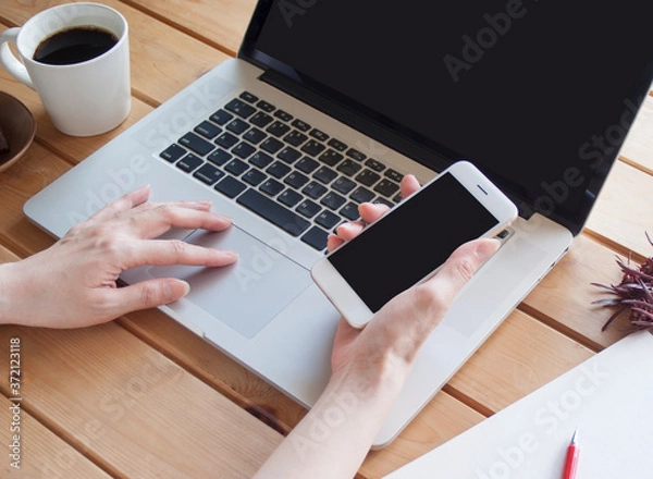 Obraz スマートフォンを片手にパソコンを操作する女性