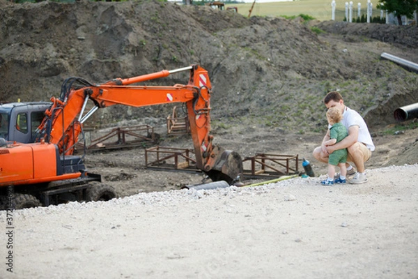 Obraz A young father and son on a construction site. They look at the excavator.